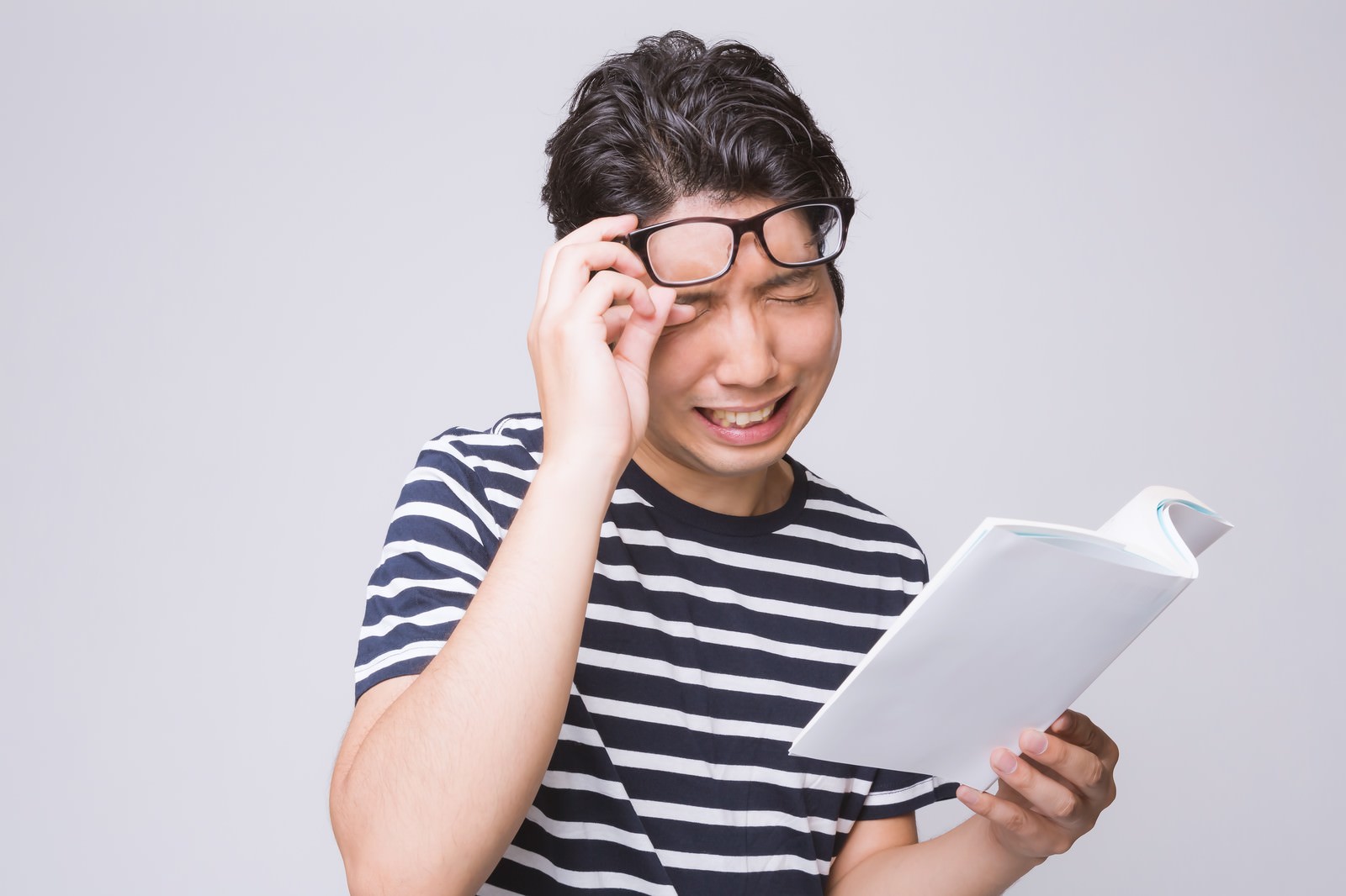 本を読んで感動して泣き笑いする眼鏡をかけた男性［モデル：紳さん］