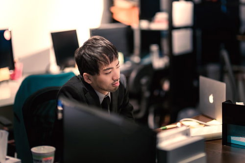 オフィスで孤独にパソコンで残業する男性