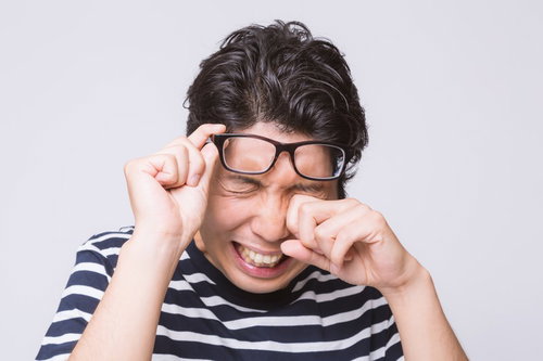 眼鏡を触りながら泣き笑いする男性