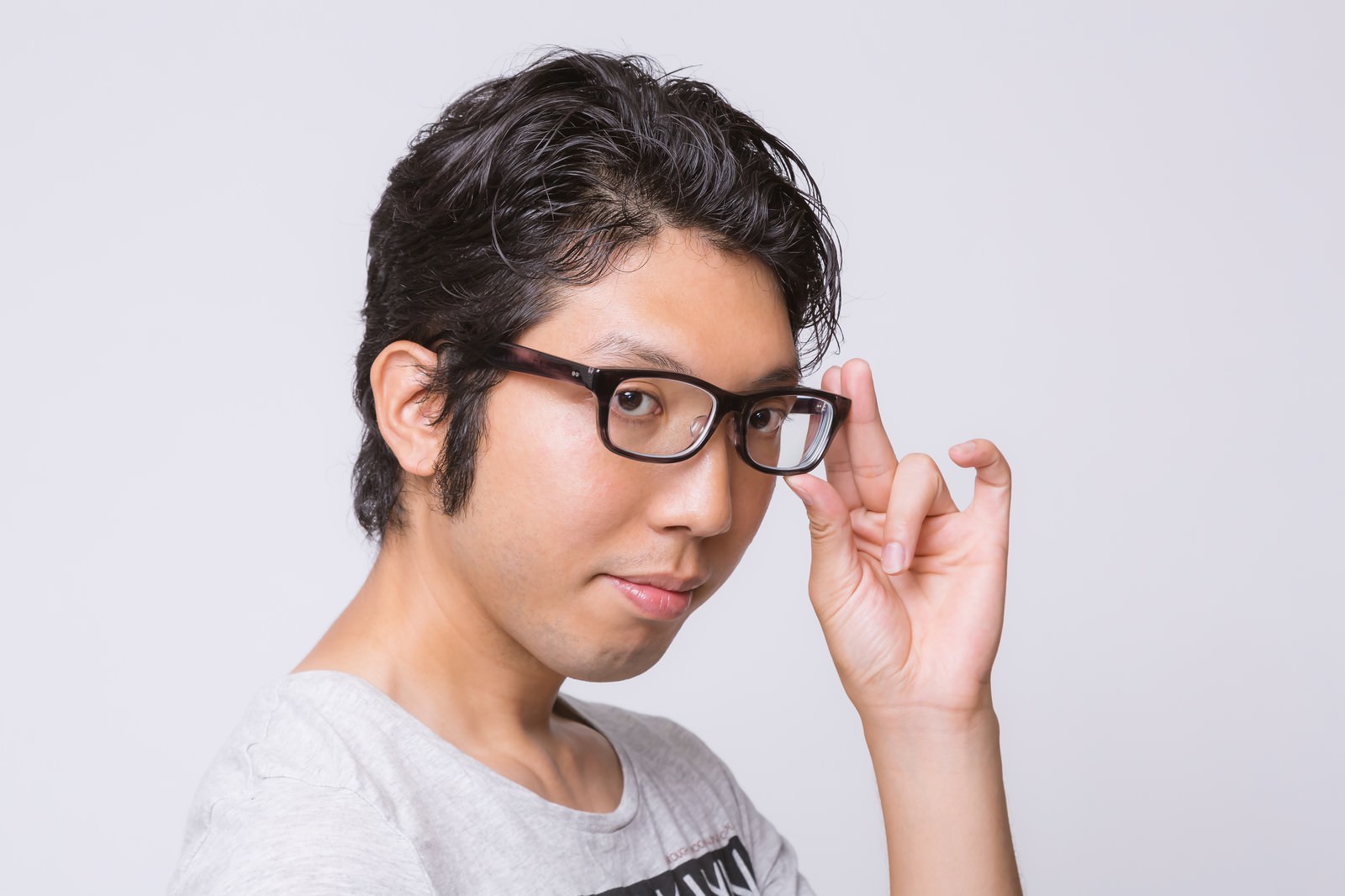 黒縁眼鏡をかけた男性が右手で眼鏡を直しながら、自信ありげに微笑む横顔のポートレート［モデル：紳さん］