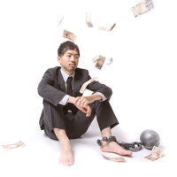 鉄球につながれ降ってくるお金を見つめる社畜の写真