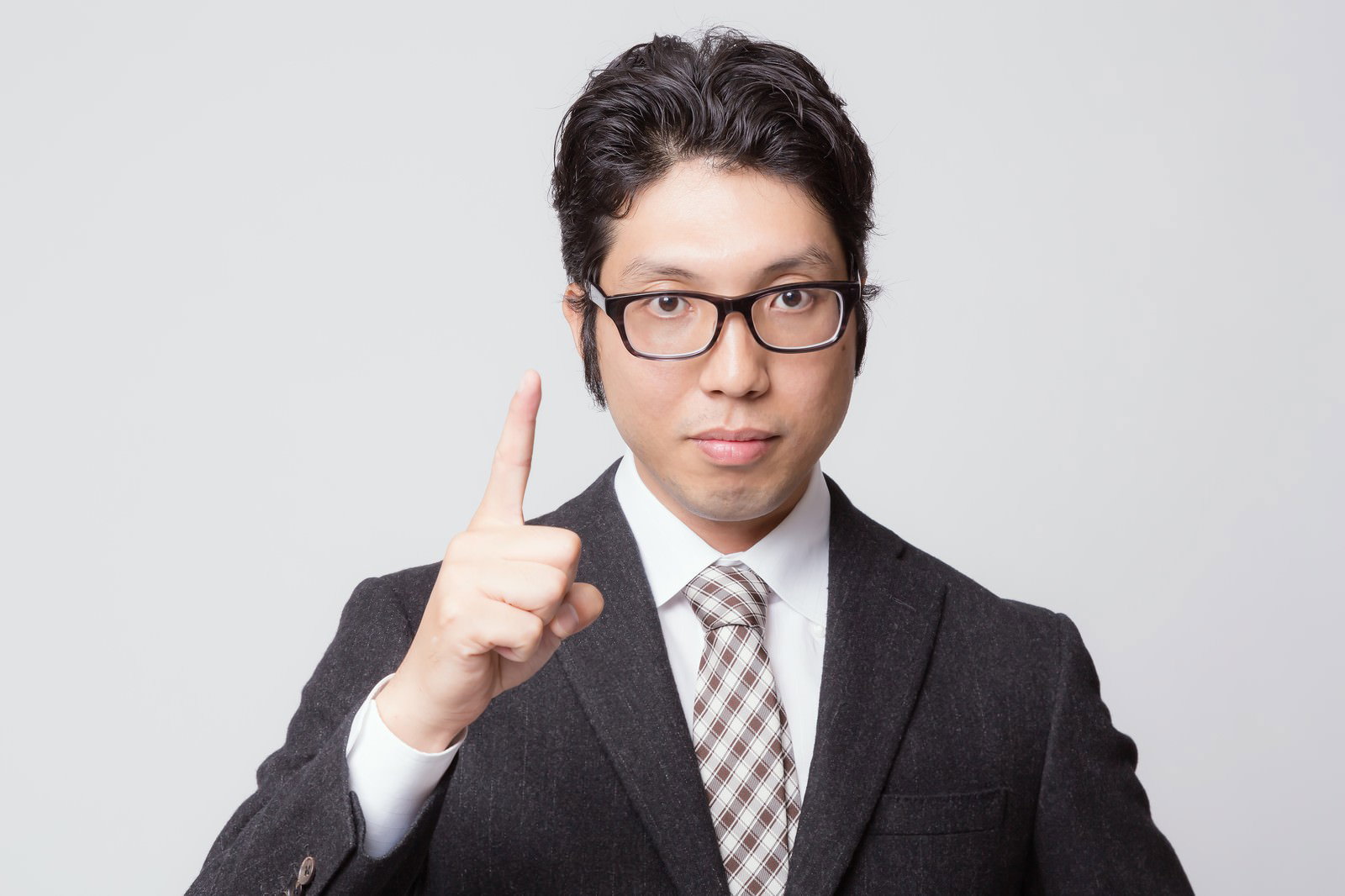 グレーのスーツと黒縁眼鏡の男性が、左手の人差し指を立てて指している［モデル：紳さん］