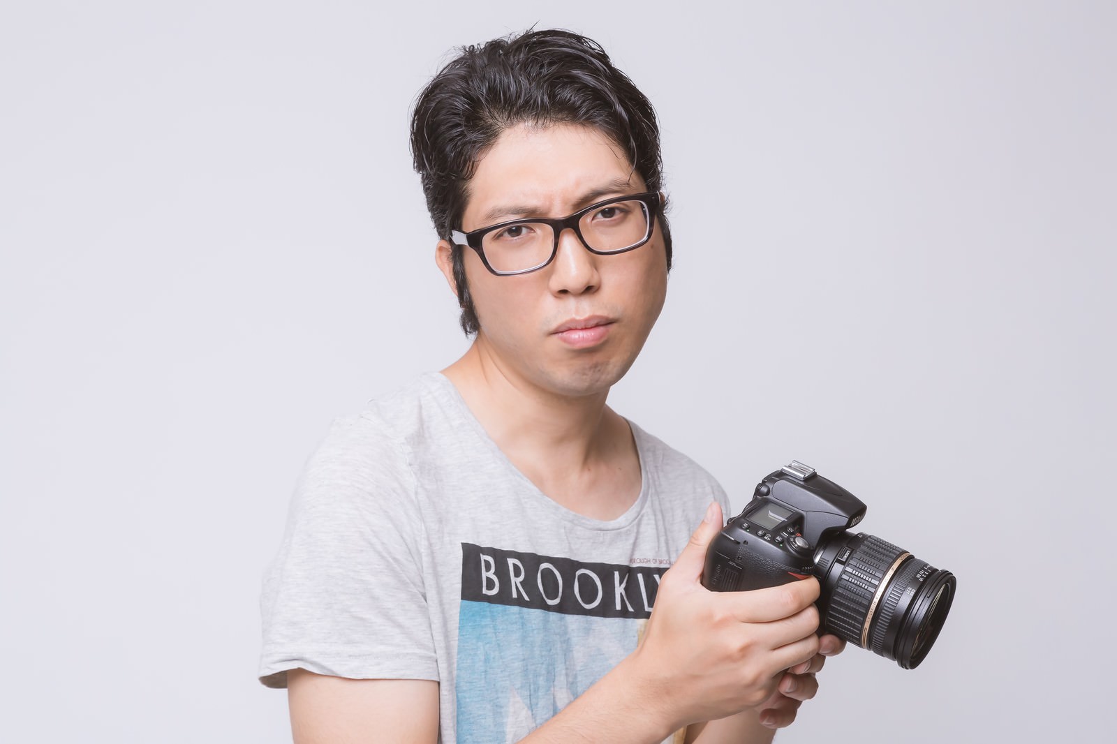 一眼レフカメラを持って困った表情の眼鏡をかけた男性［モデル：紳さん］