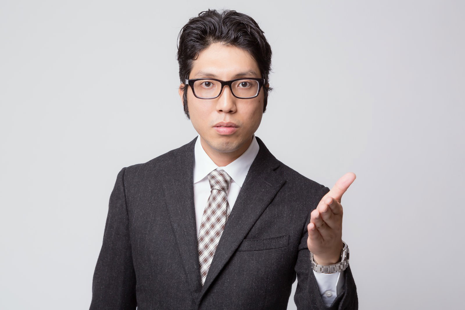 グレーのスーツと眼鏡をかけた男性営業マンが右手の指を立てながら指差している［モデル：紳さん］