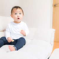 ソファーの上で想定外に戸惑う赤ちゃん、留守番中のひとコマの写真