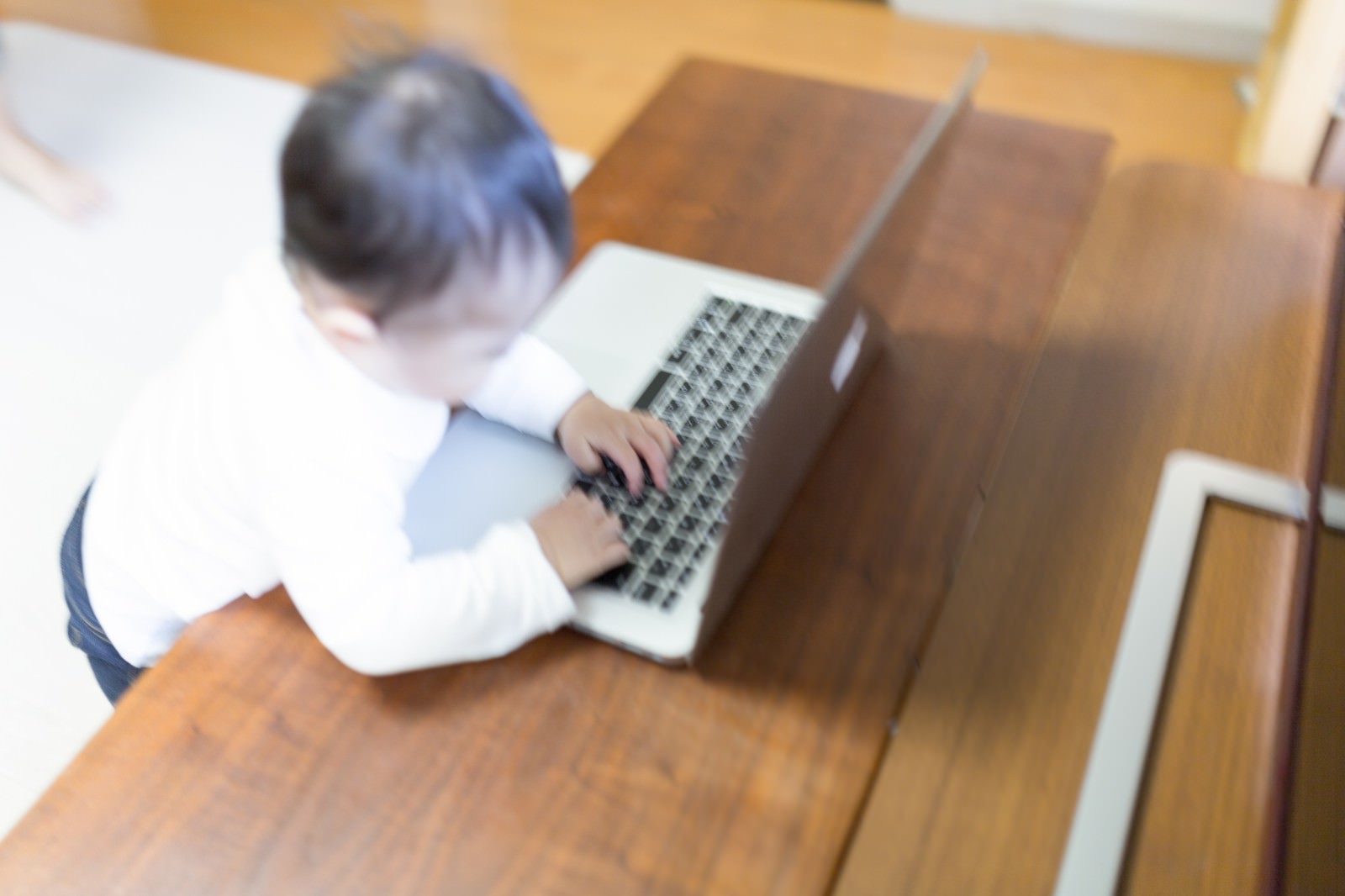白い長袖の赤ちゃんがパソコンのキーボードに両手を置き操作している［モデル：Lisa］
