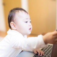 パソコンのキーボードに手を伸ばす赤ちゃんの写真