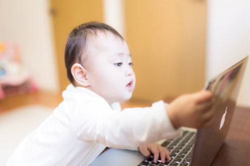 パソコンのキーボードに手を伸ばす赤ちゃん