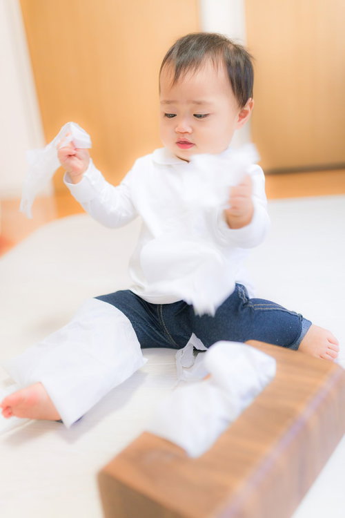 床に座って白いティッシュを散らかす白い服と青ジーンズの子供