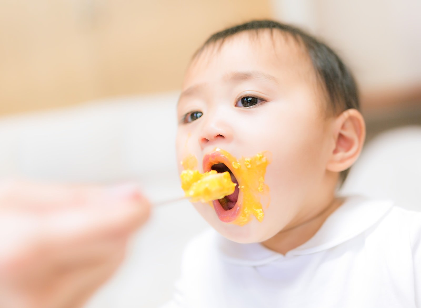大人の手のスプーンから黄色い離乳食を食べる赤ちゃん［モデル：Lisa］