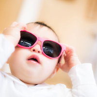 ピンクのサングラスを手で触りながらかける赤ちゃんの写真