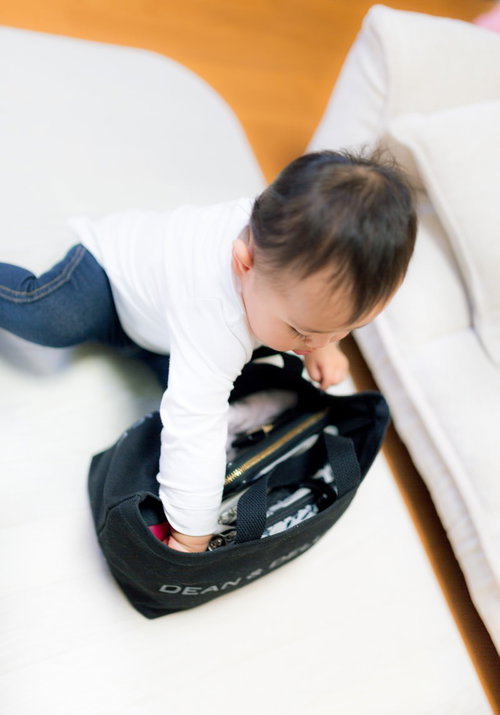 白いソファで黒いDEAN & DELUCAバッグの中を覗く幼児