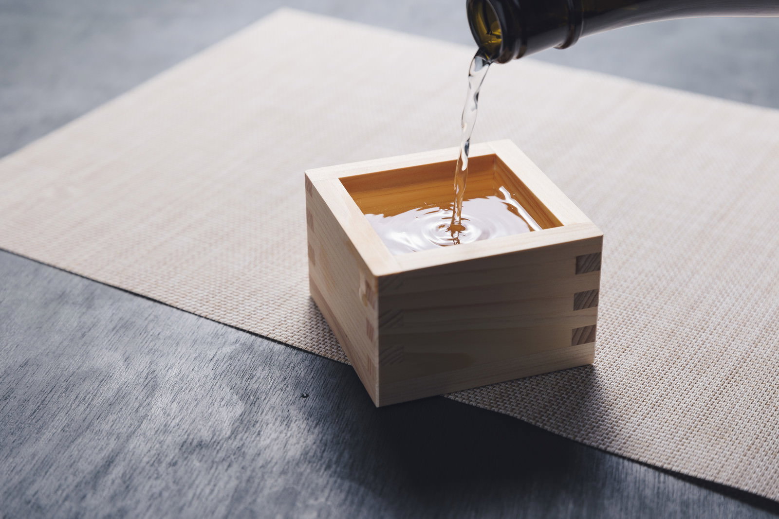木製の升に日本酒が注がれている瞬間を撮影した写真