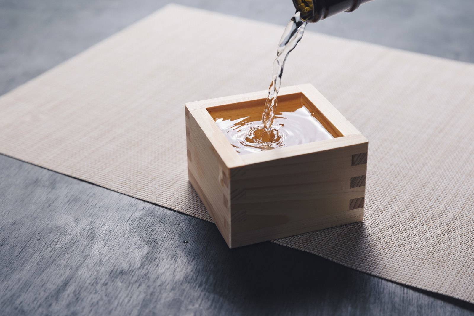 木製の升に徳利から日本酒を注いでいる様子
