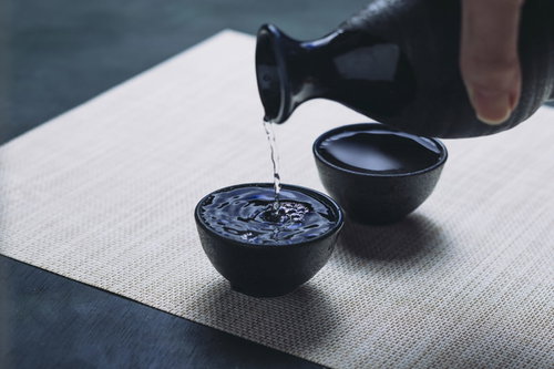 黒い徳利からお猪口に注がれた日本酒の