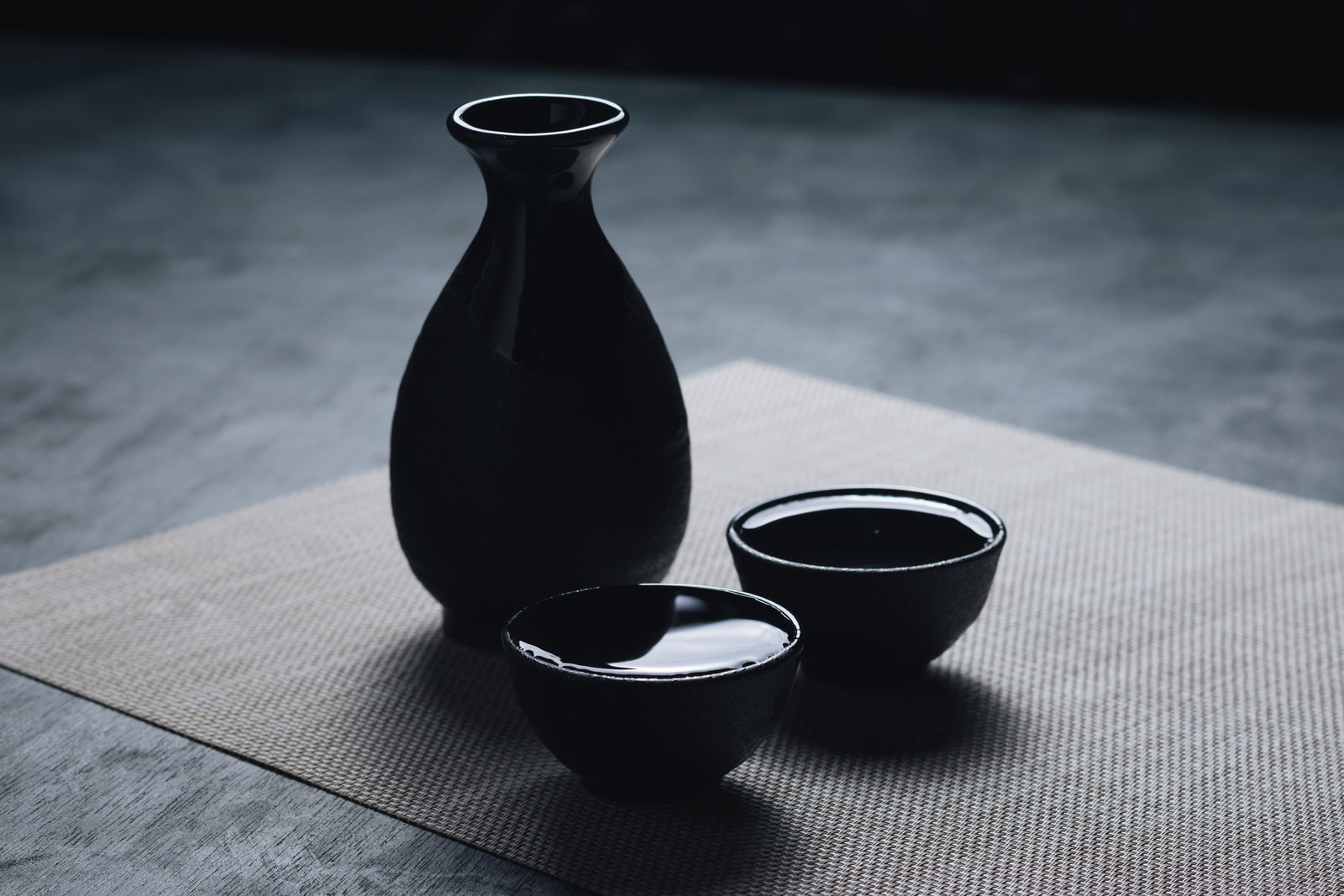 黒い徳利と白いお猪口に表面張力でなみなみと注がれた日本酒
