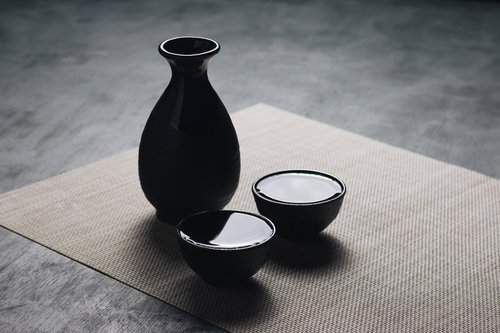 黒い徳利とお猪口になみなみの日本酒