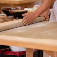 生地を丁寧に木製めん棒で巻き上げる蕎麦打ち職人の写真