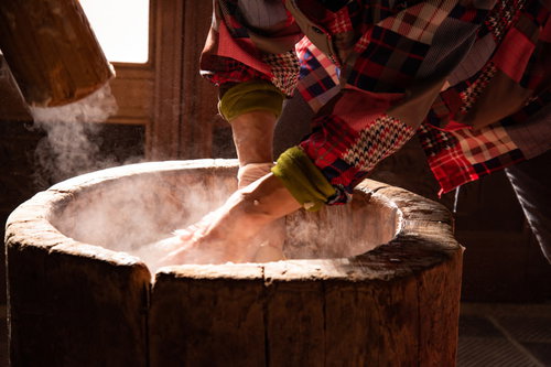 つきたての餅をなでるおばあちゃんの手と木製の臼