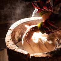 湯気が立ち上る臼で餅を回すベテランの手つき技の写真