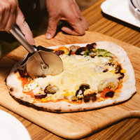 カッティングボードに乗せられたピザをピザカッターで切り分けるの写真