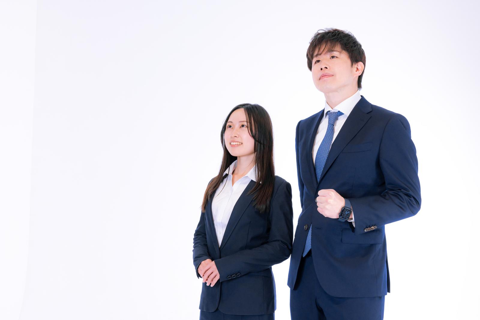 紺色のスーツを着た男性と女性のM&Aアドバイザーが並んで立つ［モデル：野崎繁裕 吉屋ゆり］