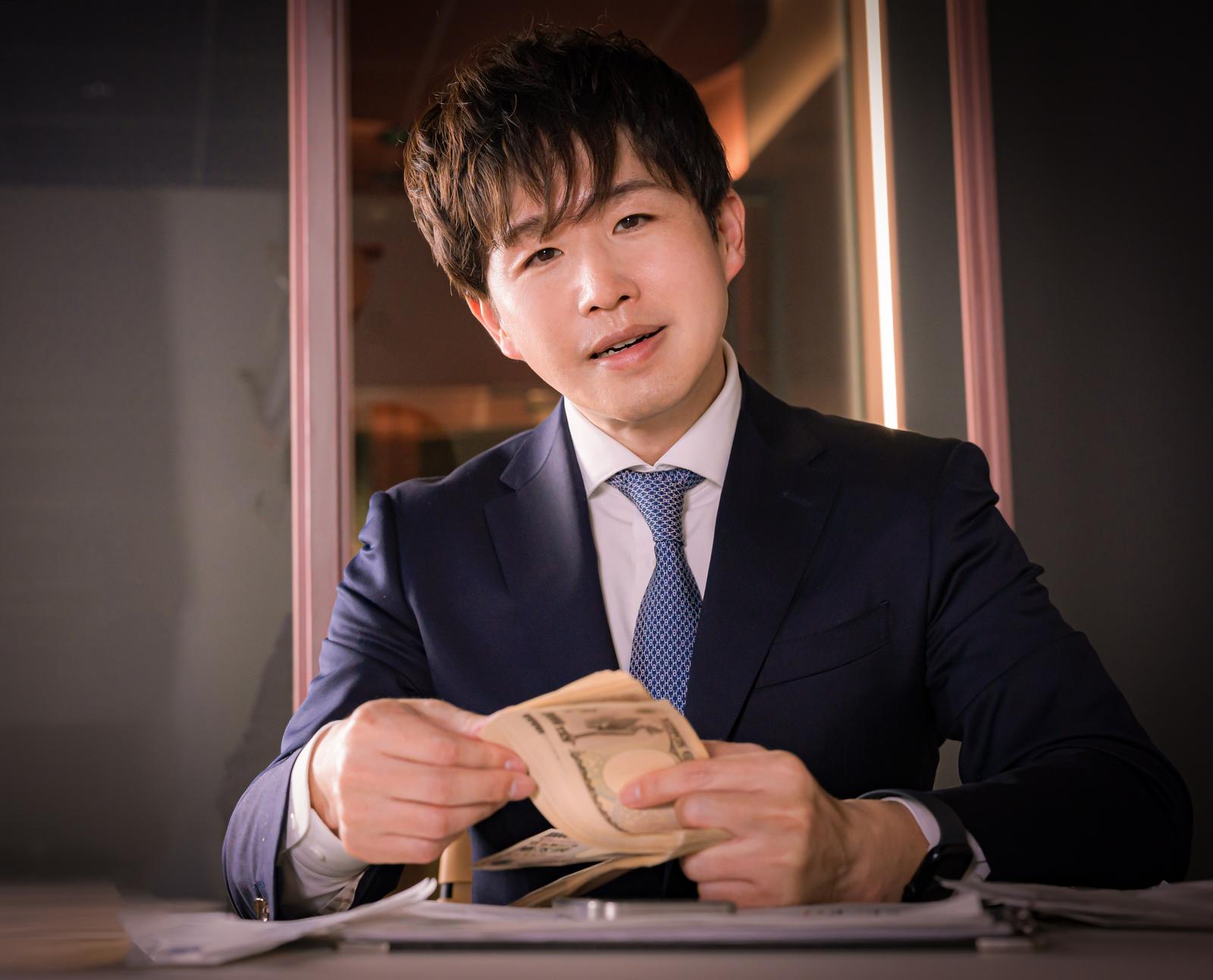 スーツの男性が紙幣の束を持つビジネスシーン［モデル：野崎繁裕］