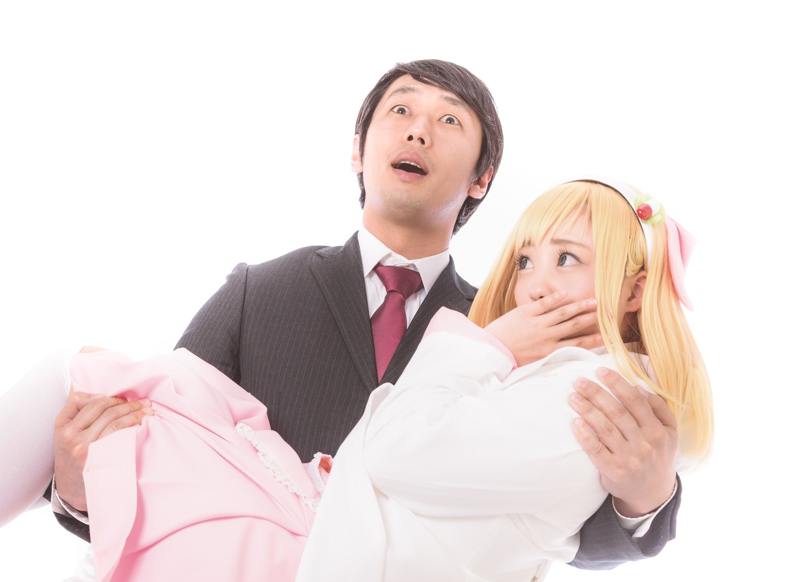 白い背景で金髪かつらの人物をお姫様抱っこするスーツの男性［モデル：大川竜弥 河村友歌］