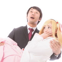金髪かつらの人物をお姫様抱っこするスーツの男性の写真