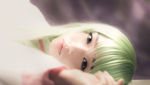 柔らかい光の室内で横たわりこちらを見つめる緑色の髪のコスプレの人物