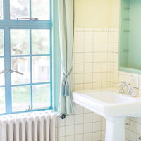 白いタイル壁と窓がある明るい浴室の洗面台の写真