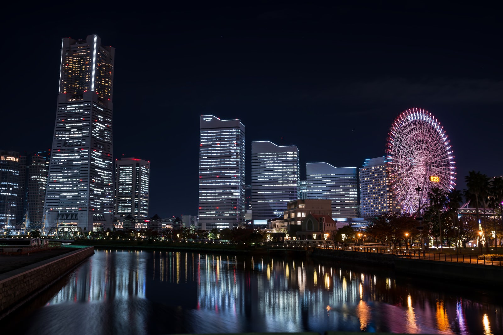 夜のみなとみらいの河川越しの景観。左側に照明がついた高層ビル、右奥にピンクに輝く観覧車が見える