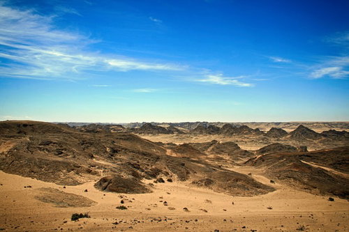 青空が広がる広大な荒野と岩肌の大地、丘陵地帯の風景