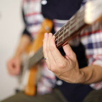 ベーシストの左手元でフレットを押さえる演奏シーンの写真