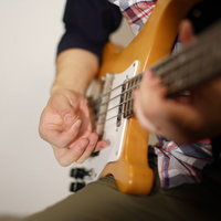 黄色いベースギターをピックで弾くベーシストの手元の写真