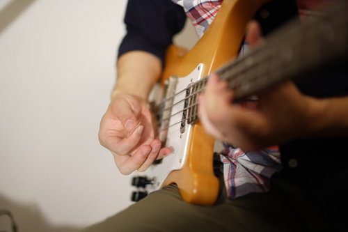 黄色いベースギターをピックで弾くベーシストの手元