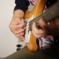 ピック弾きするベーシストの手元の演奏風景の写真