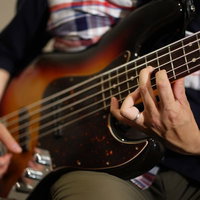 難しいハイポジションを押さえて演奏するベーシストの写真