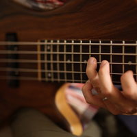 5弦ベースのフレットを押さえるベーシストの左手の写真