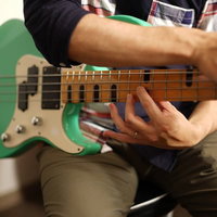 チェックシャツを着た男性ベーシストが緑色のエレキベースを弾くの写真