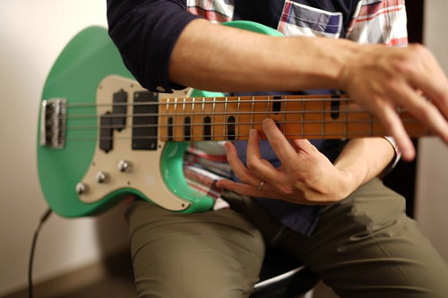 チェックシャツを着た男性ベーシストが緑色のエレキベースを弾く