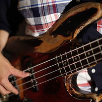 チェック柄シャツを着たベーシストのベース演奏の手元の写真