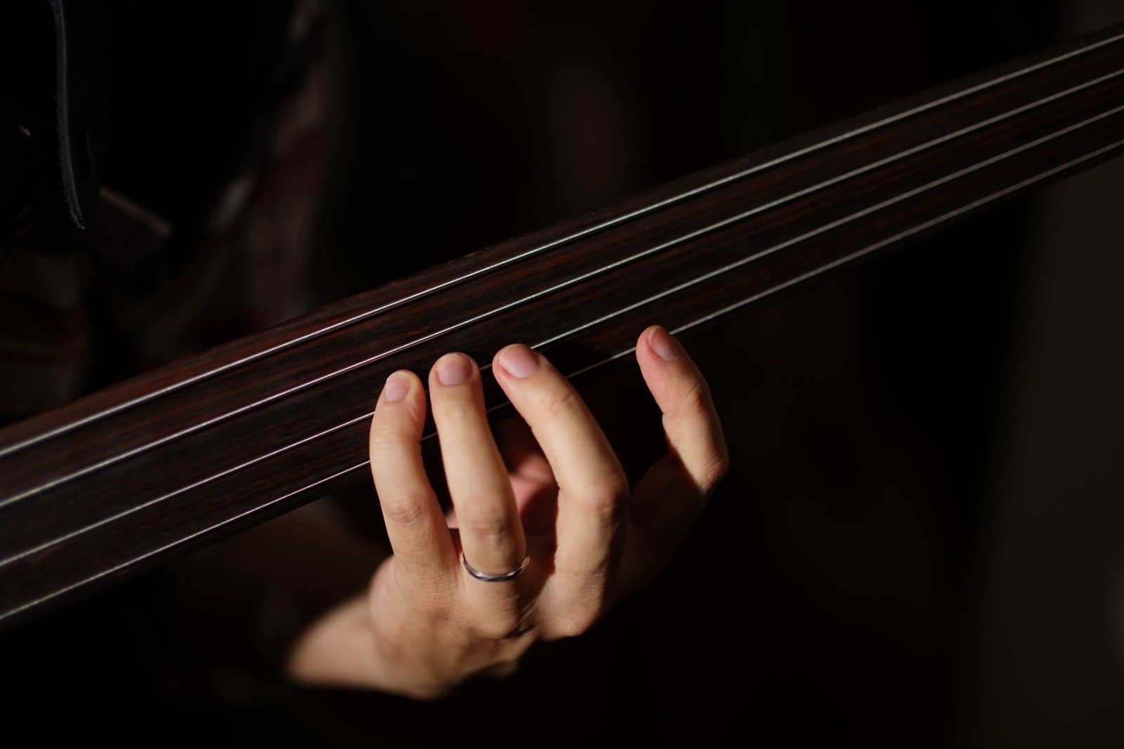 暗い背景でフレットレスベースの弦を押さえる左手