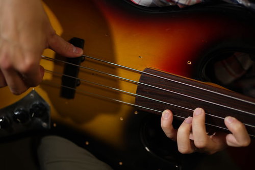 サンバーストカラーのエレキベースを指弾きするベーシストの手元