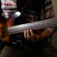 室内でベース練習をするベーシストの手元と全身の写真