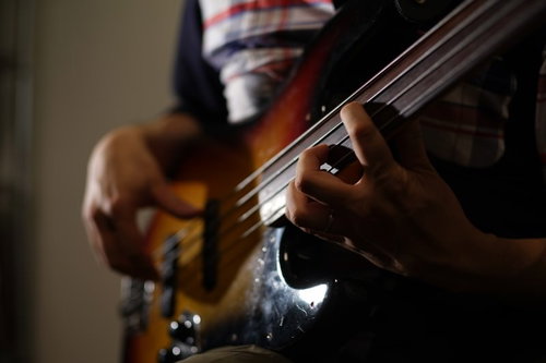 暗い照明の中でベースギターの弦を丁寧に押さえる演奏者の手元