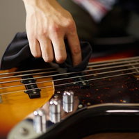 クロスでベースの弦を一本ずつ拭くメンテナンスの写真