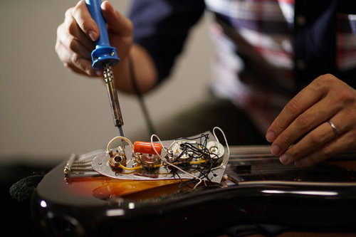 ピックガードを外したエレキベースの電子部品をメンテナンスする作業