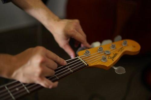 オレンジ色のベースの弦の張りをチェックするベーシスト