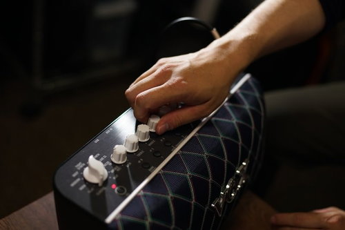 ギターアンプのツマミを指で調整する手元の操作風景